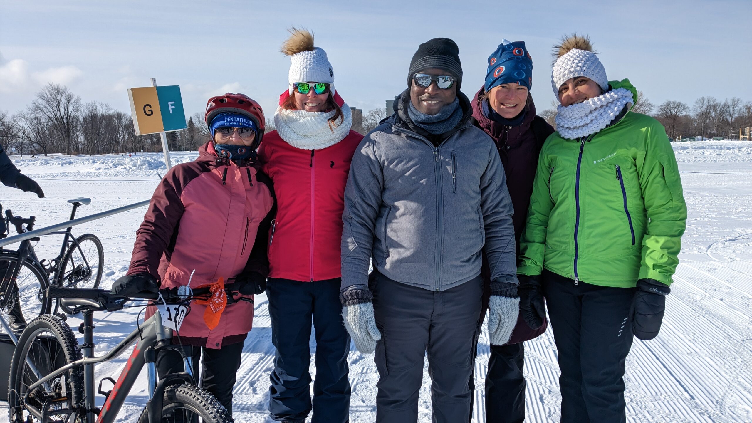 5 personnes debout côte à côte, employées de l'Institut et habillées pour l'hiver, à l'extérieur et qui sourient lors du Pentathlon des neiges