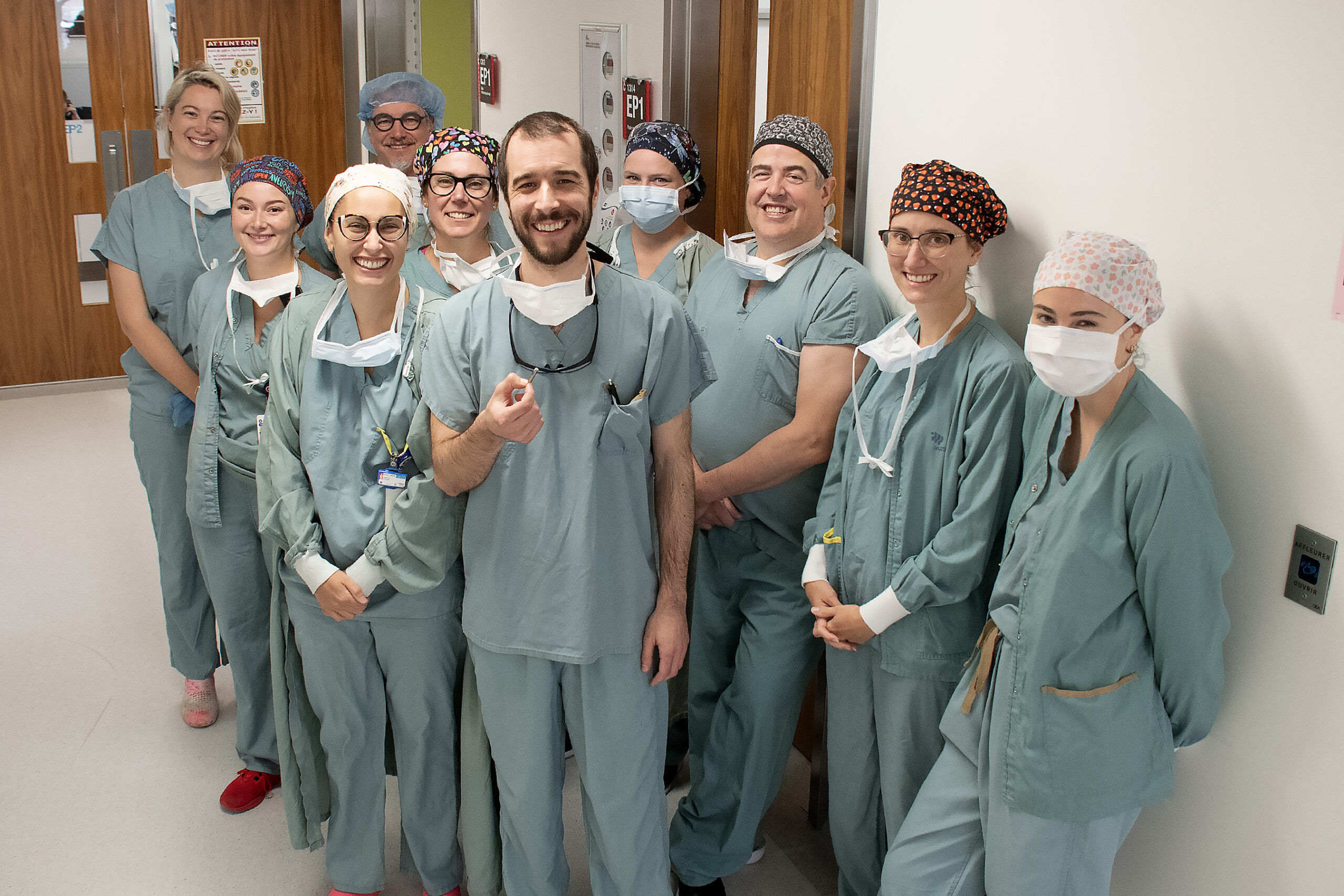 L'équipe d'hémodynamie et d'électrophysiologie, en uniforme vert, sourient. Dr Pierre-Hugo Racine, à l'avant, tient dans sa main le cardiostimulation à double sonde.